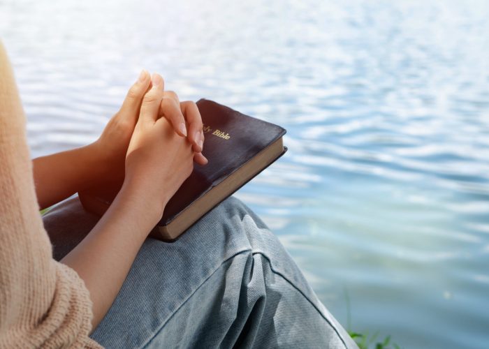 Woman hands holding bible and praying at river in the morning